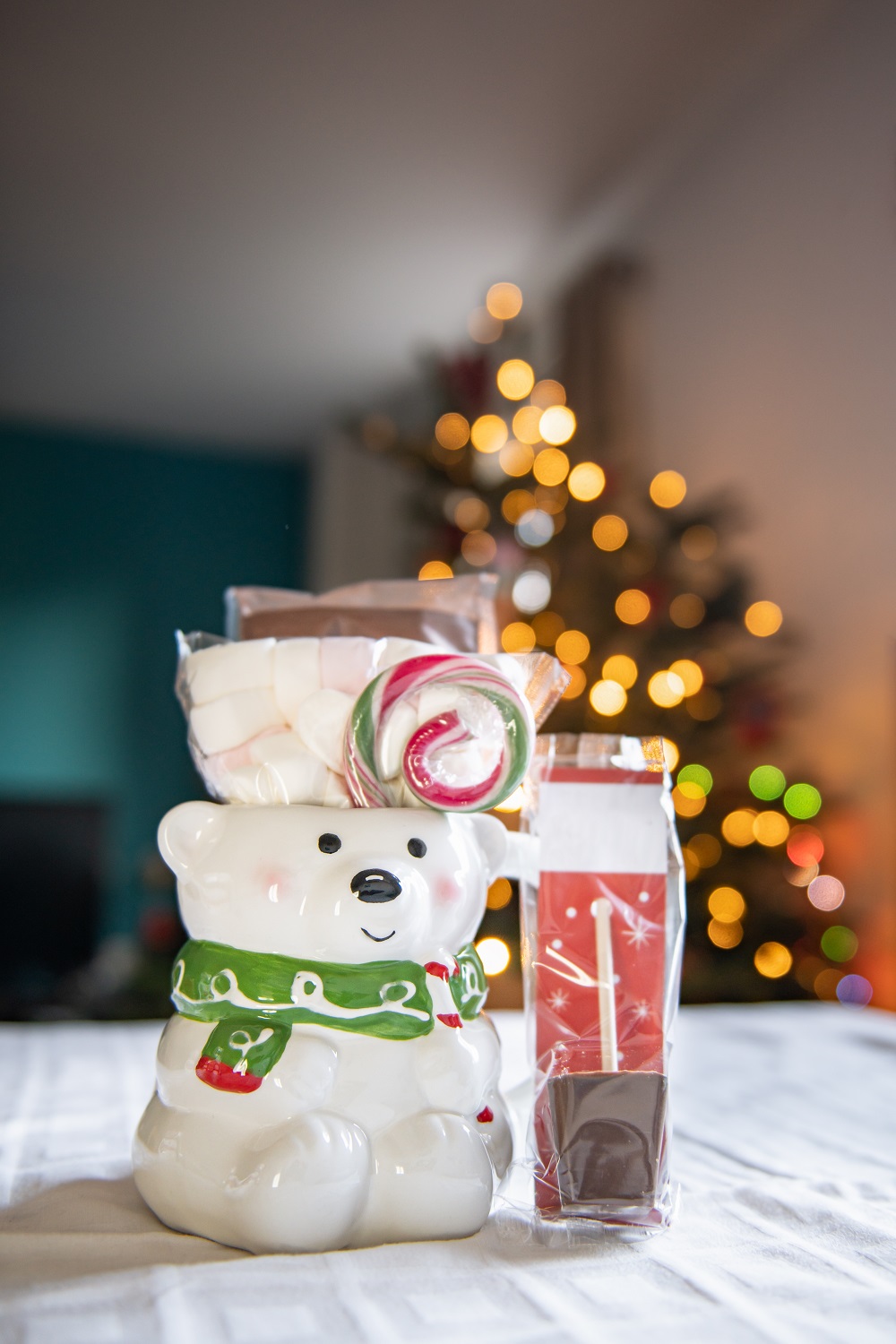 Christmas gift set made with 3d Snowman mug and cacao ingredients with marshmallow and candy canes. Xmas tree with bokeh lights on the background