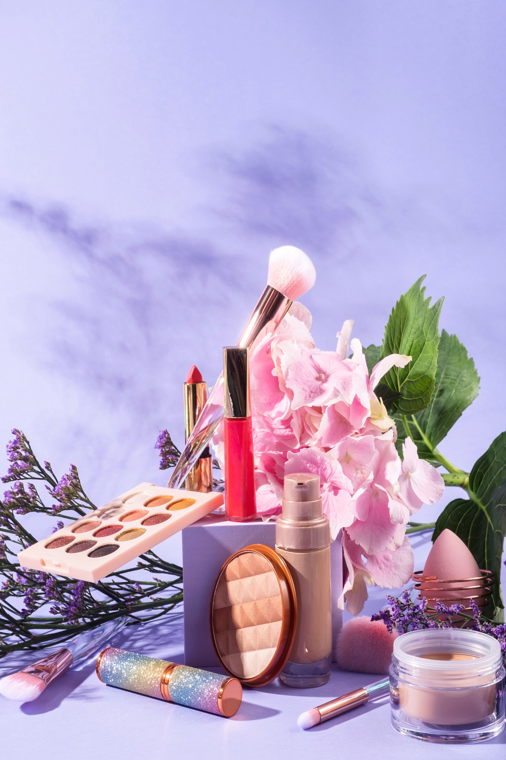 Make up products with brushes on purple geometric scene background with cube podium with pink flowers
